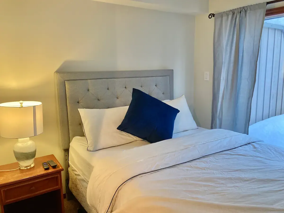 A bedroom with a bed , nightstand , lamp and window.