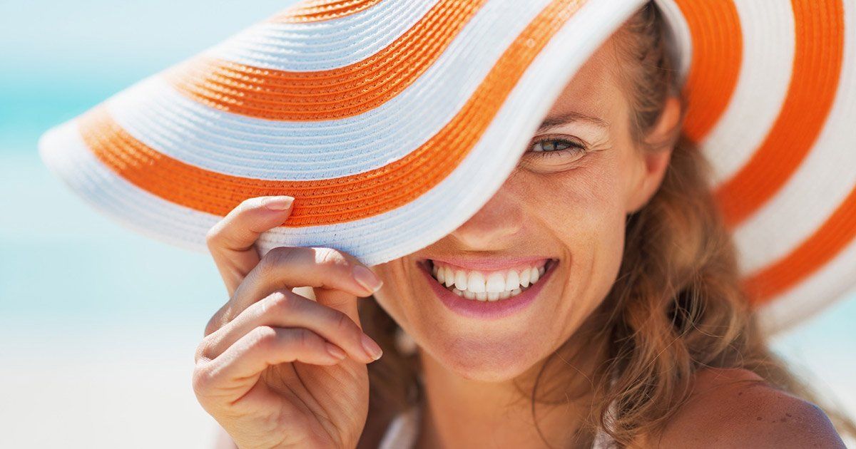 Woman smiling, wearing a large, striped orange and white sun hat on a beach.