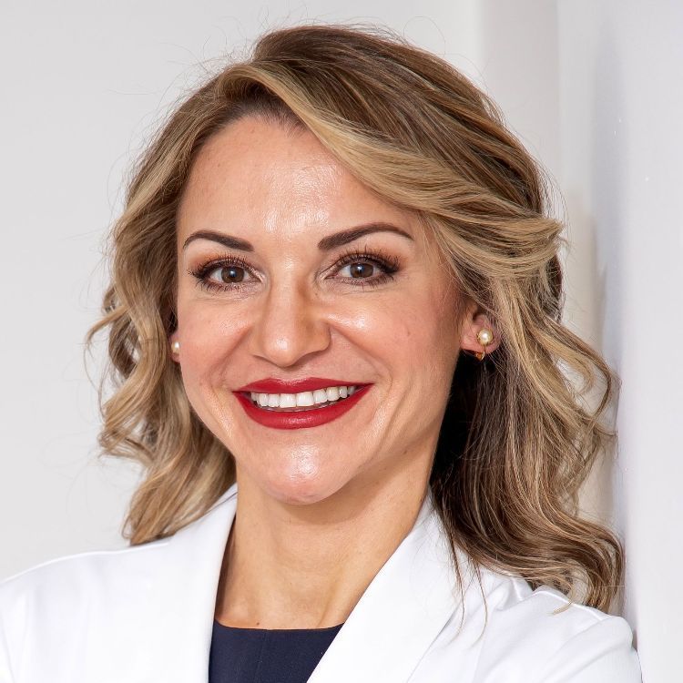 A woman wearing a white lab coat and red lipstick smiles for the camera.