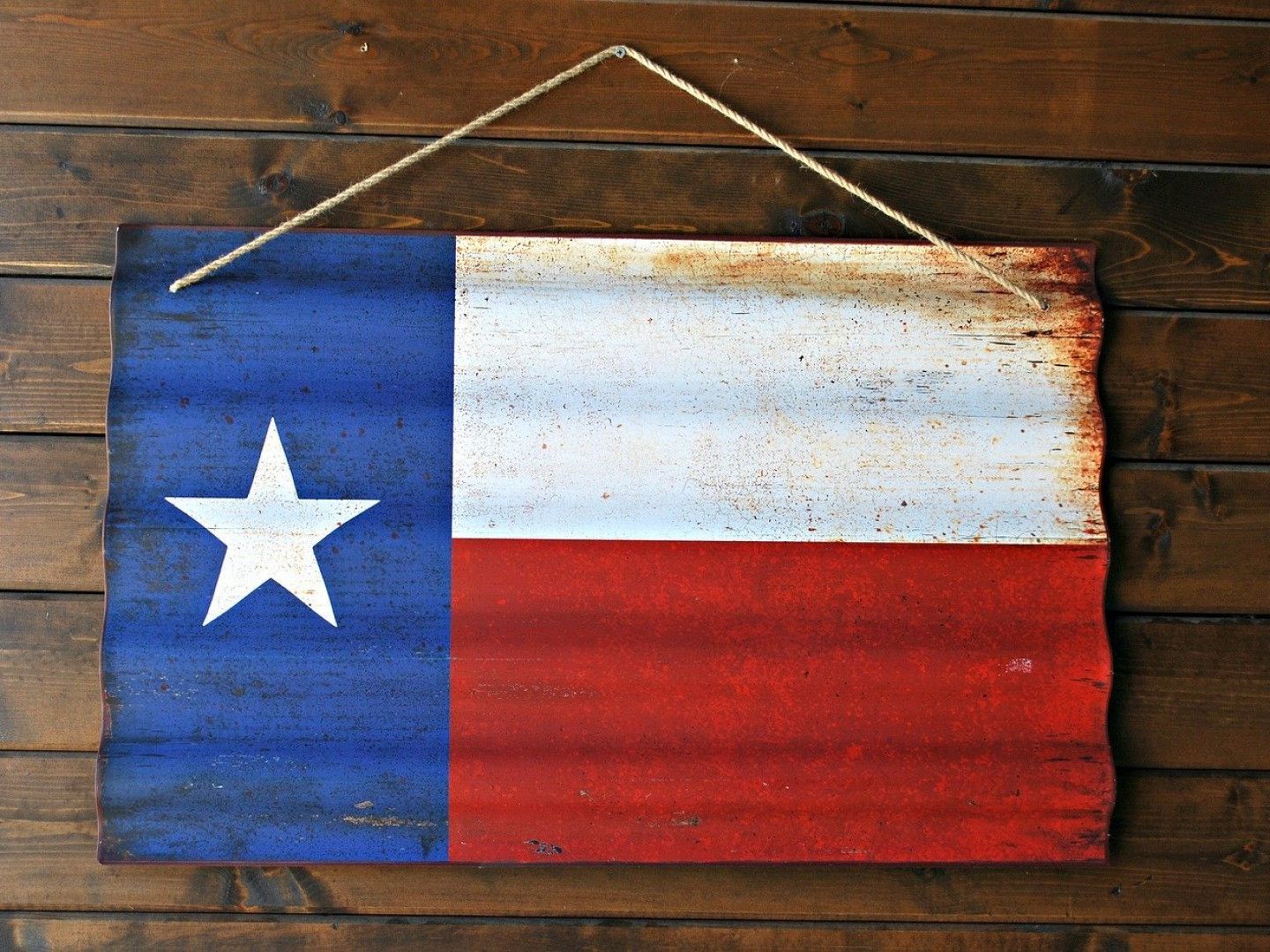 Texas flag painted on a weathered wooden plaque, hanging from a twine cord.