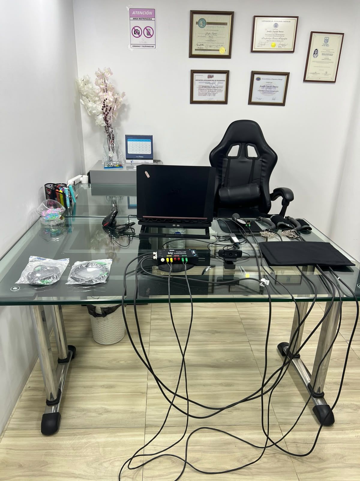 Escritorio de oficina en casa con monitor, silla de oficina y cables enredados en una habitación luminosa.