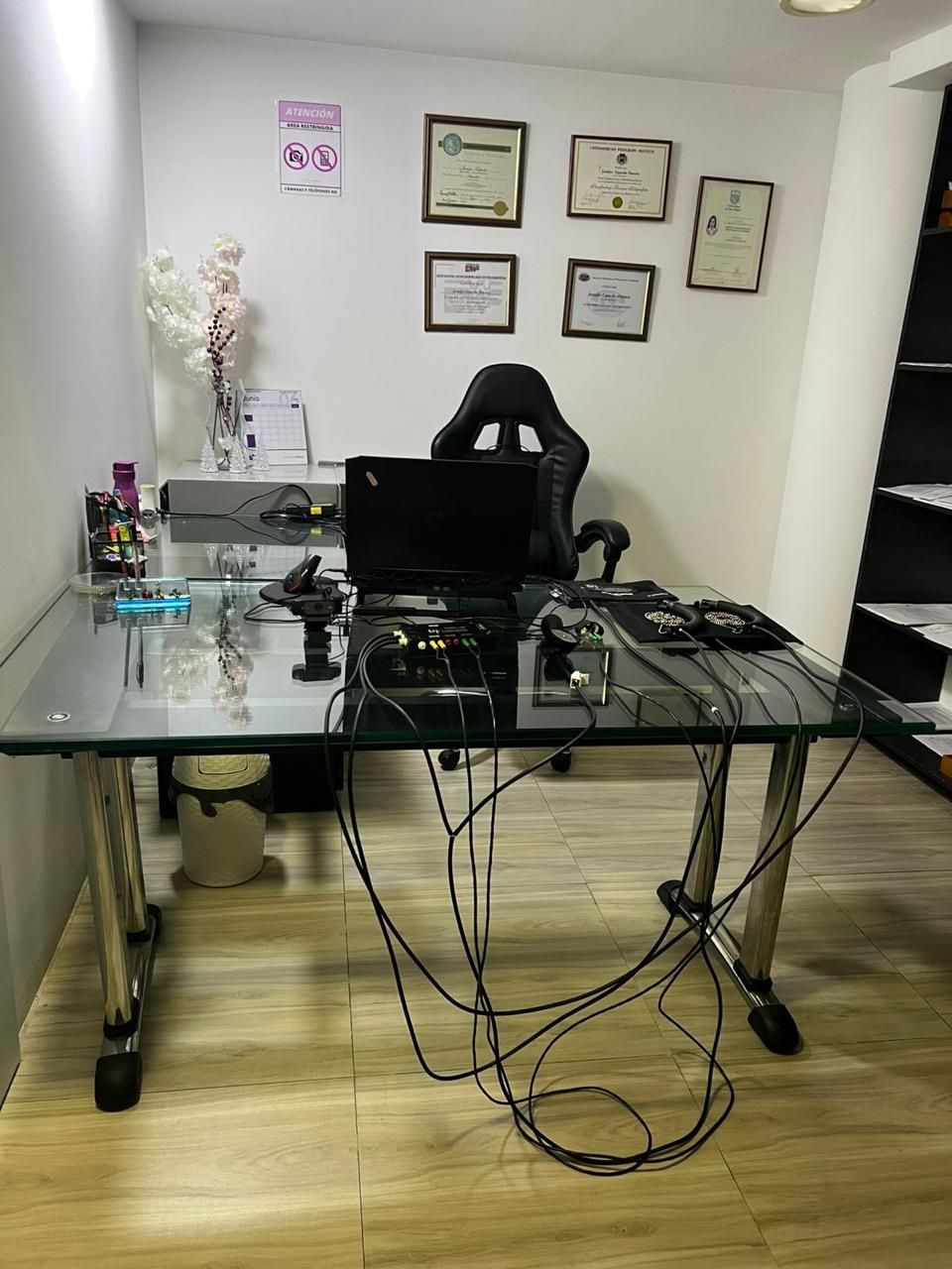 Escritorio de oficina en casa con monitor, silla de oficina y cables enredados en una habitación luminosa.