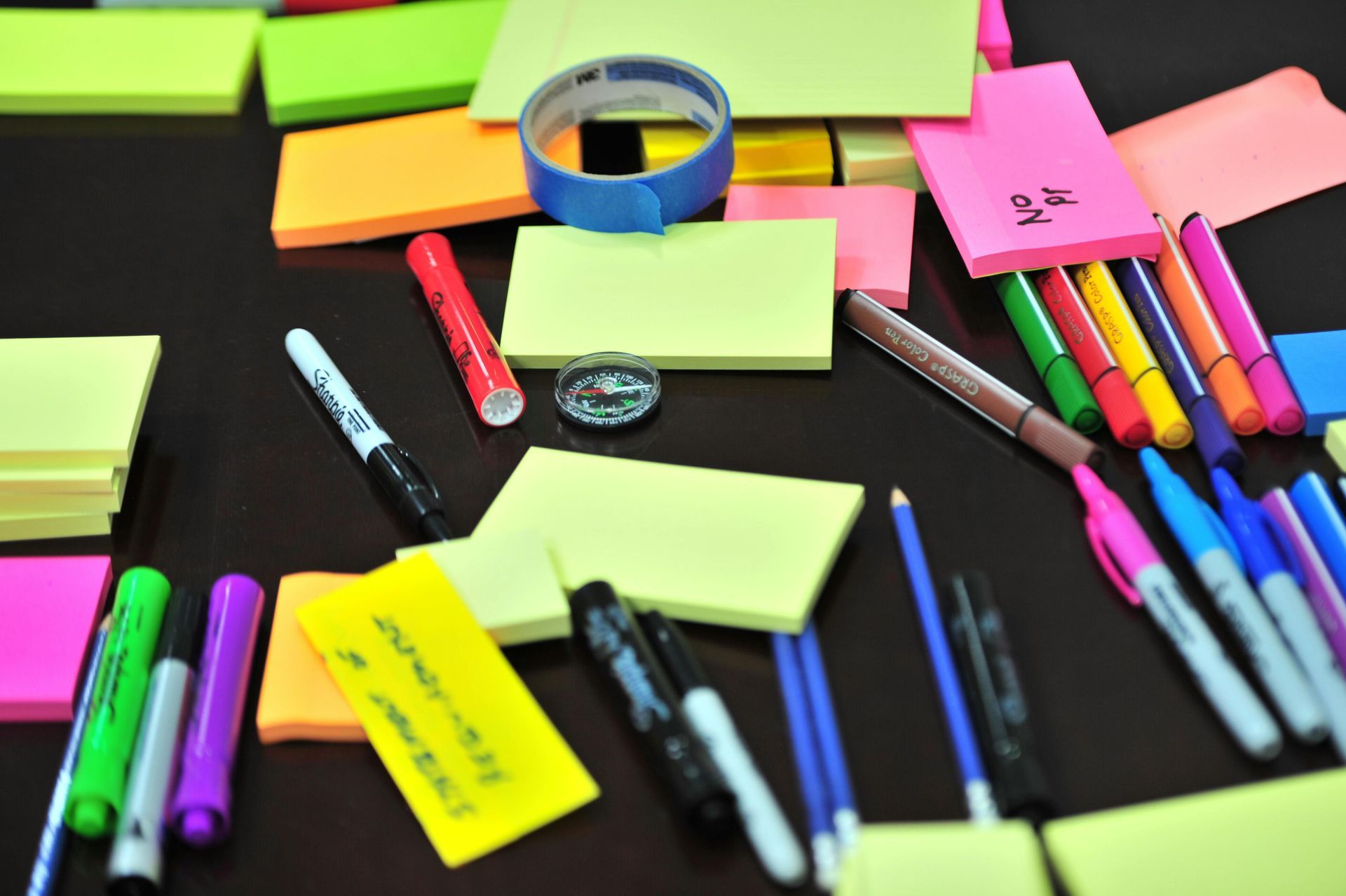 Colorful sticky notes and pens scattered on a dark surface; tools for brainstorming and organization.