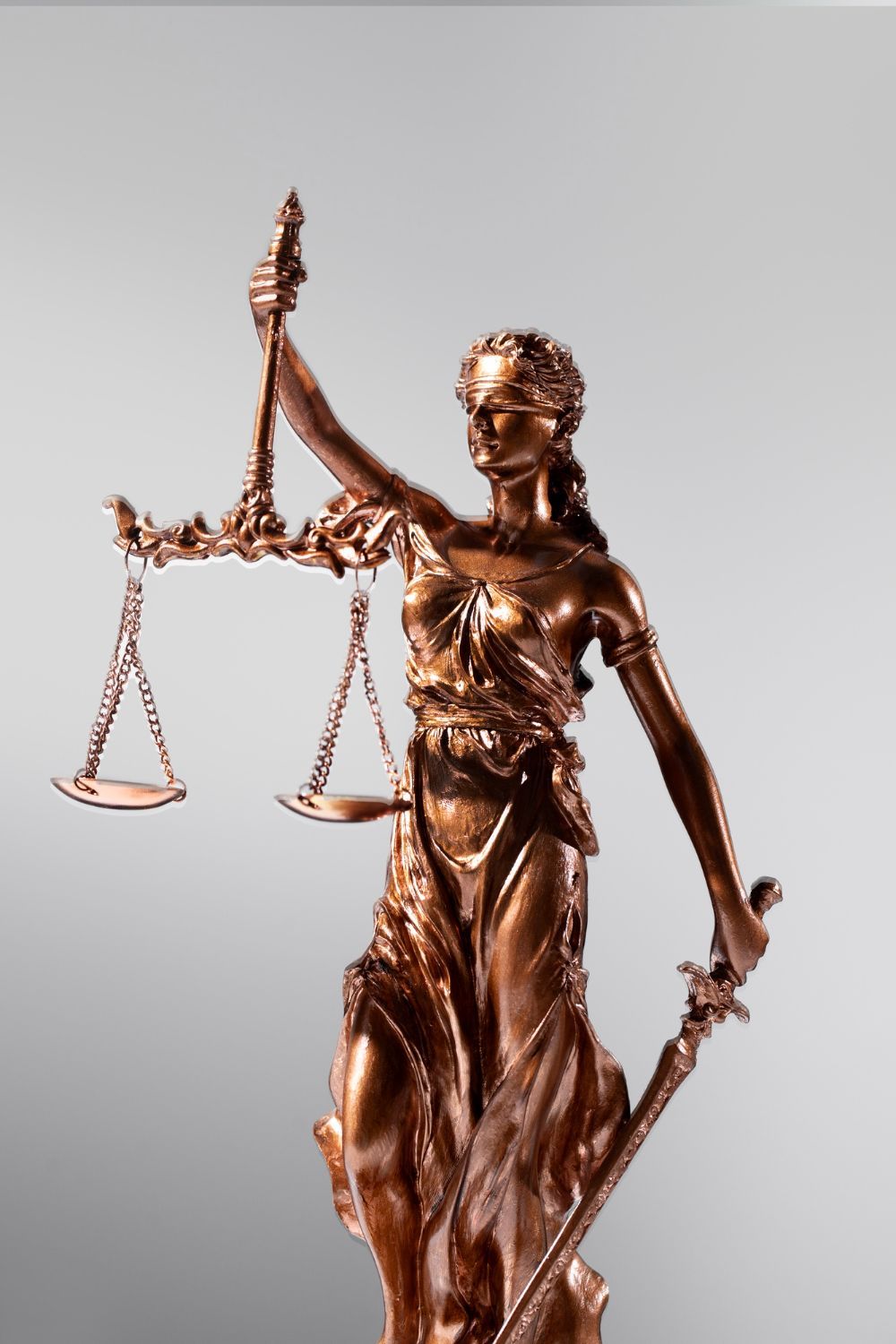Bronze Lady Justice statue holding scales and a sword against a gray background