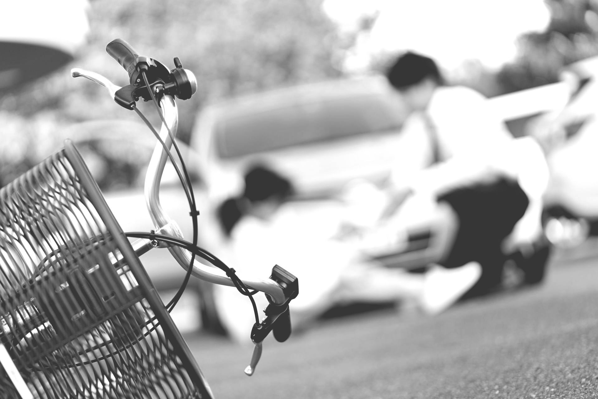 Broken bicycle lying on pavement beside a blurred scooter or motorcycle in black and white.