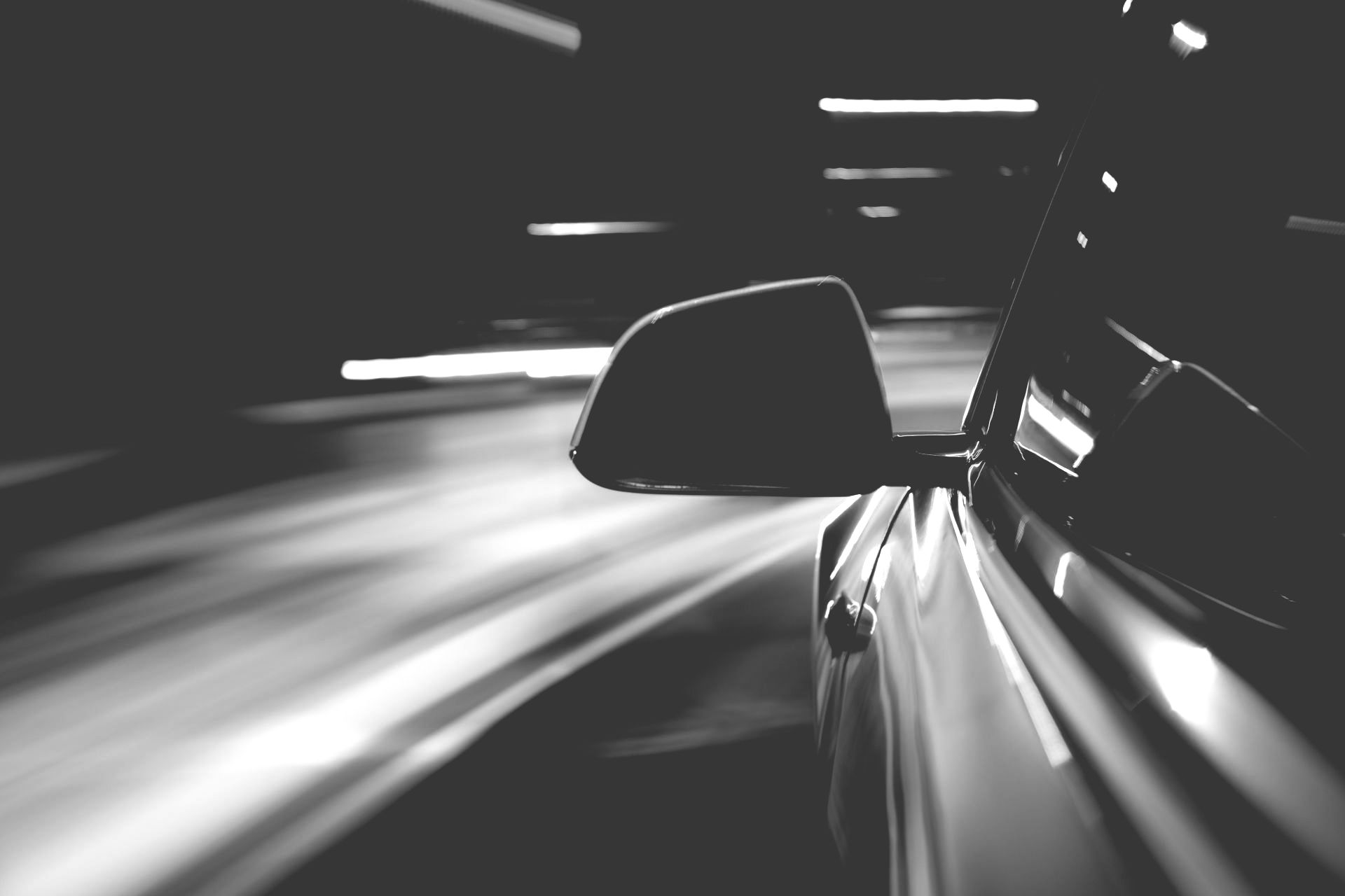 Black-and-white motion-blur view of a car driving fast at night, with side mirror visible