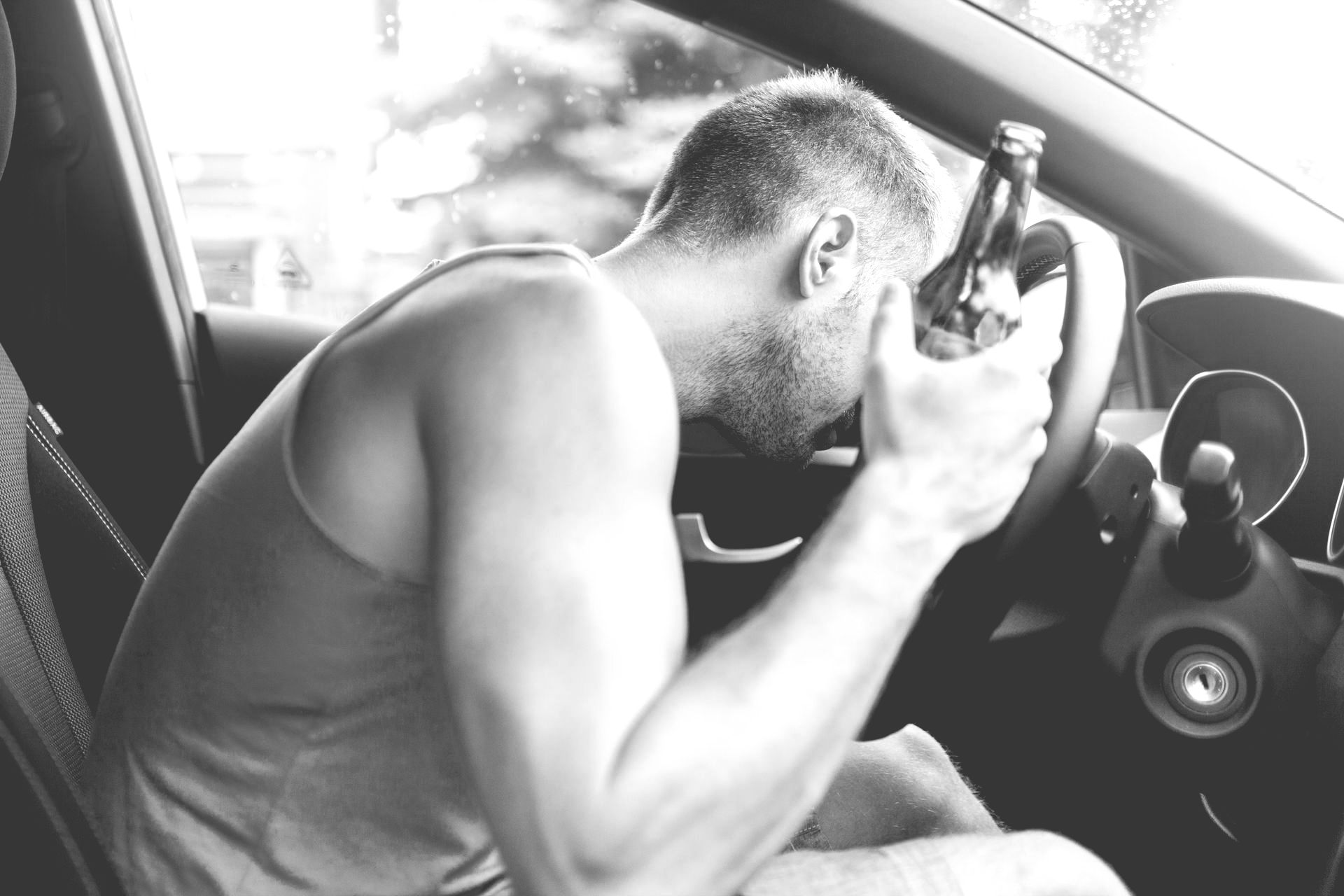 Person in a car leaning forward, holding a gun to their head in a distressed posture.