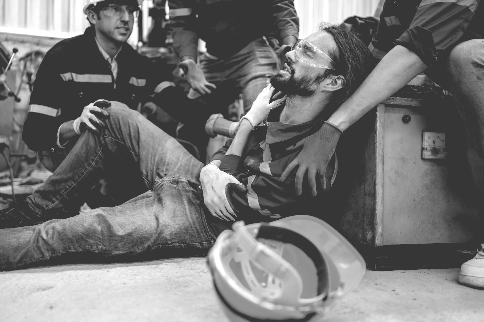 Paramedics assist an injured man lying on the ground beside a helmet in a black-and-white scene