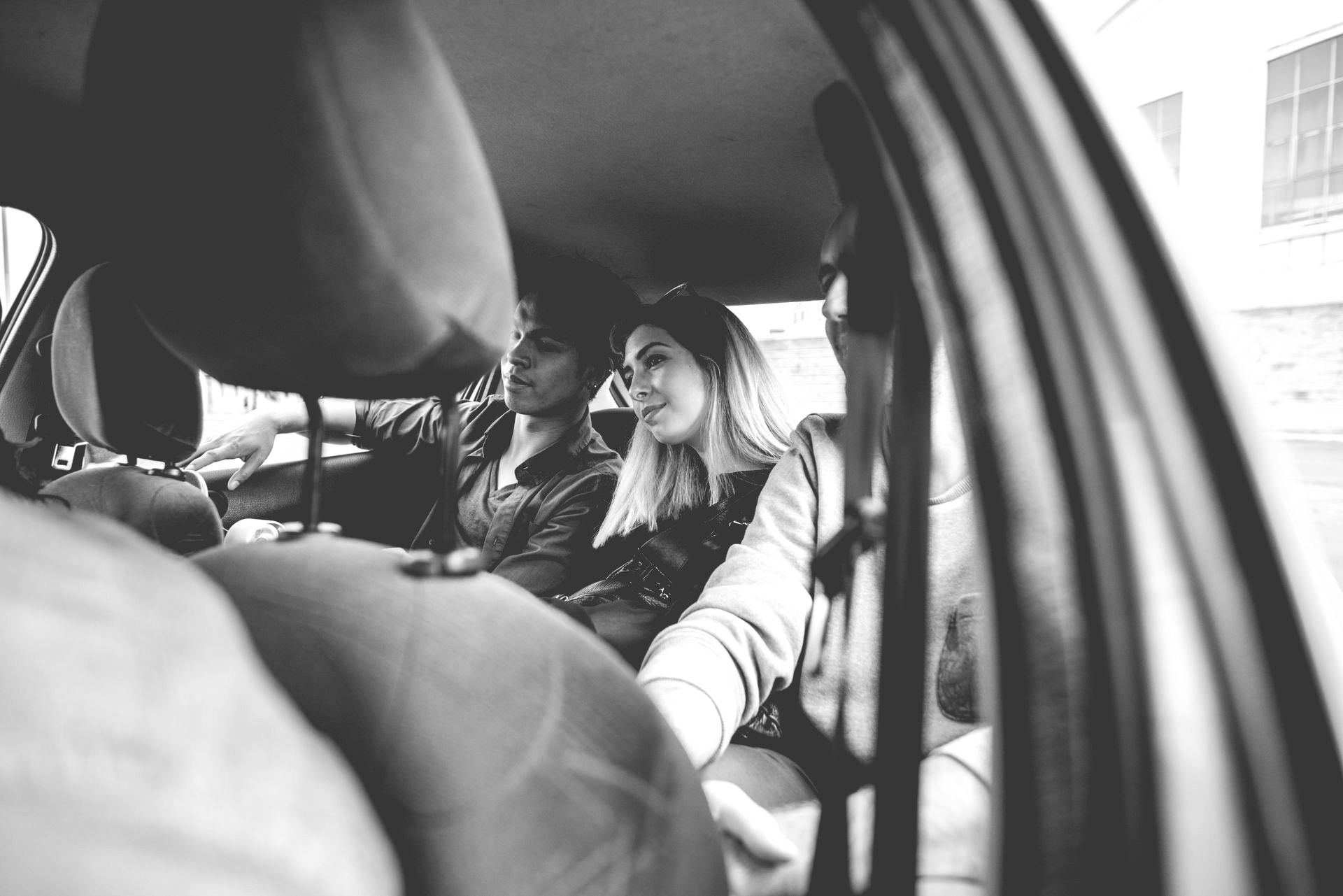 People sitting in a car, seen from the back seat, with one passenger smiling out the window.