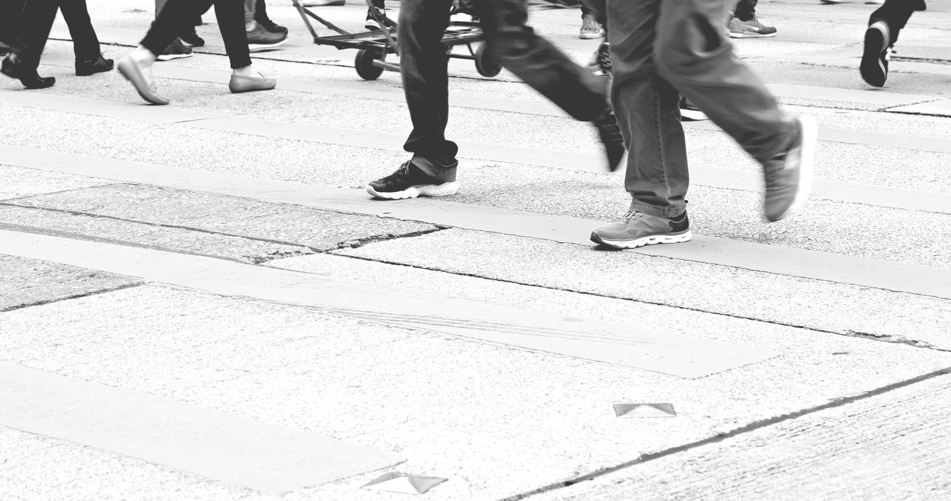 People’s feet and legs crossing a paved street in black-and-white.