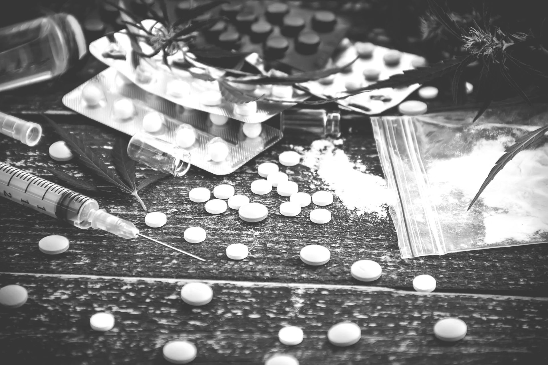 Scattered pills and a plastic bag on a dark wooden table, black-and-white scene.