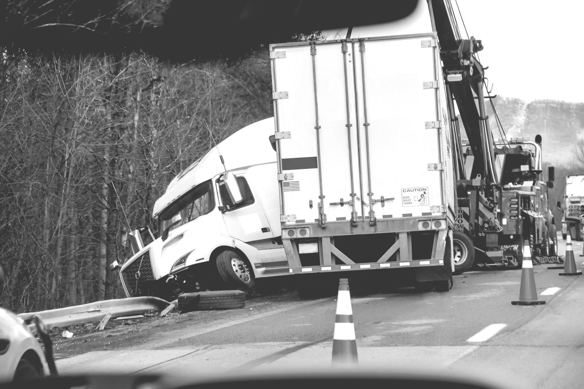Truck jackknifed on a highway, crashed into guardrail with cone and tow truck nearby