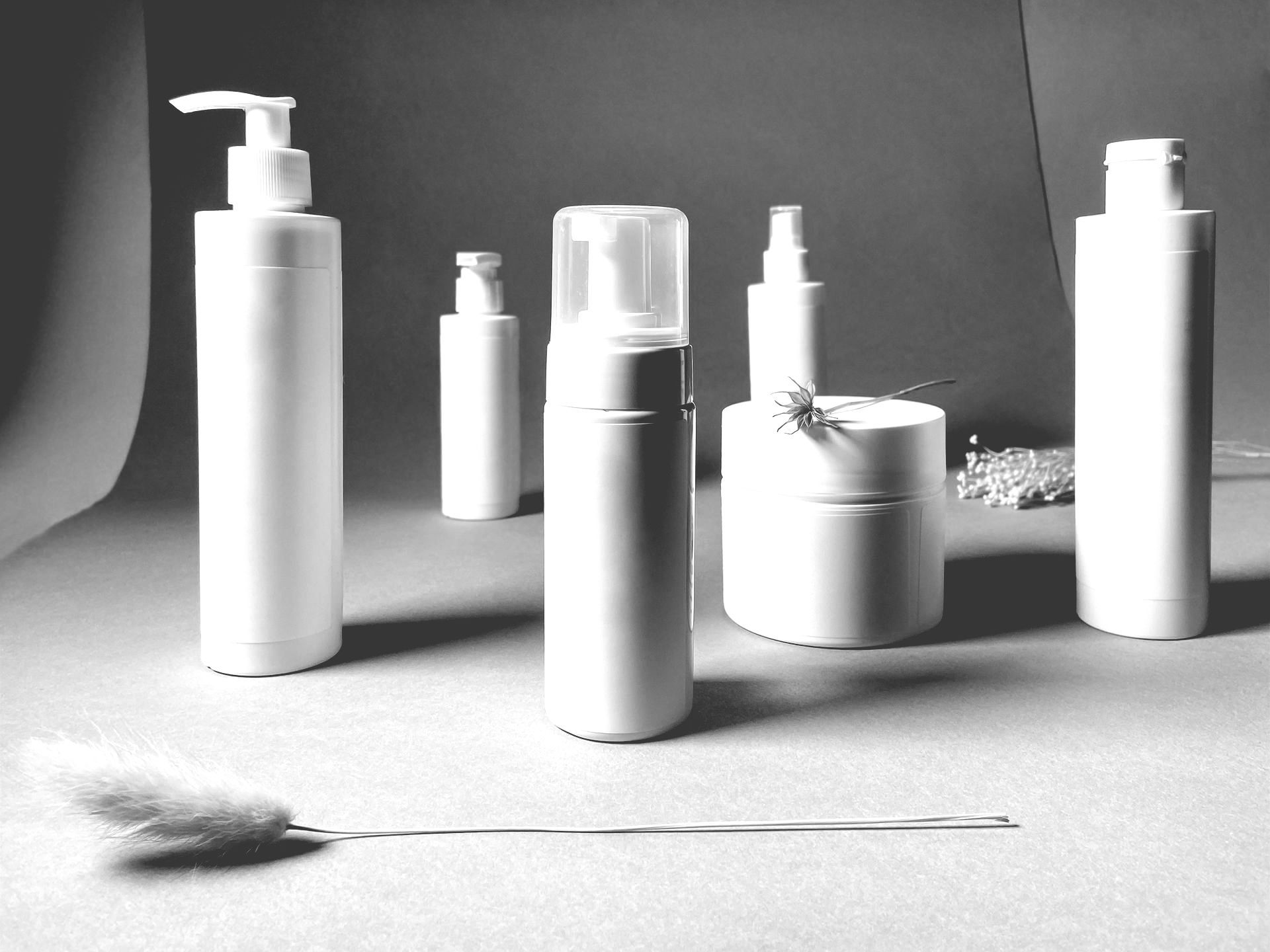 Black-and-white product display of assorted cosmetic bottles and jars on a studio surface