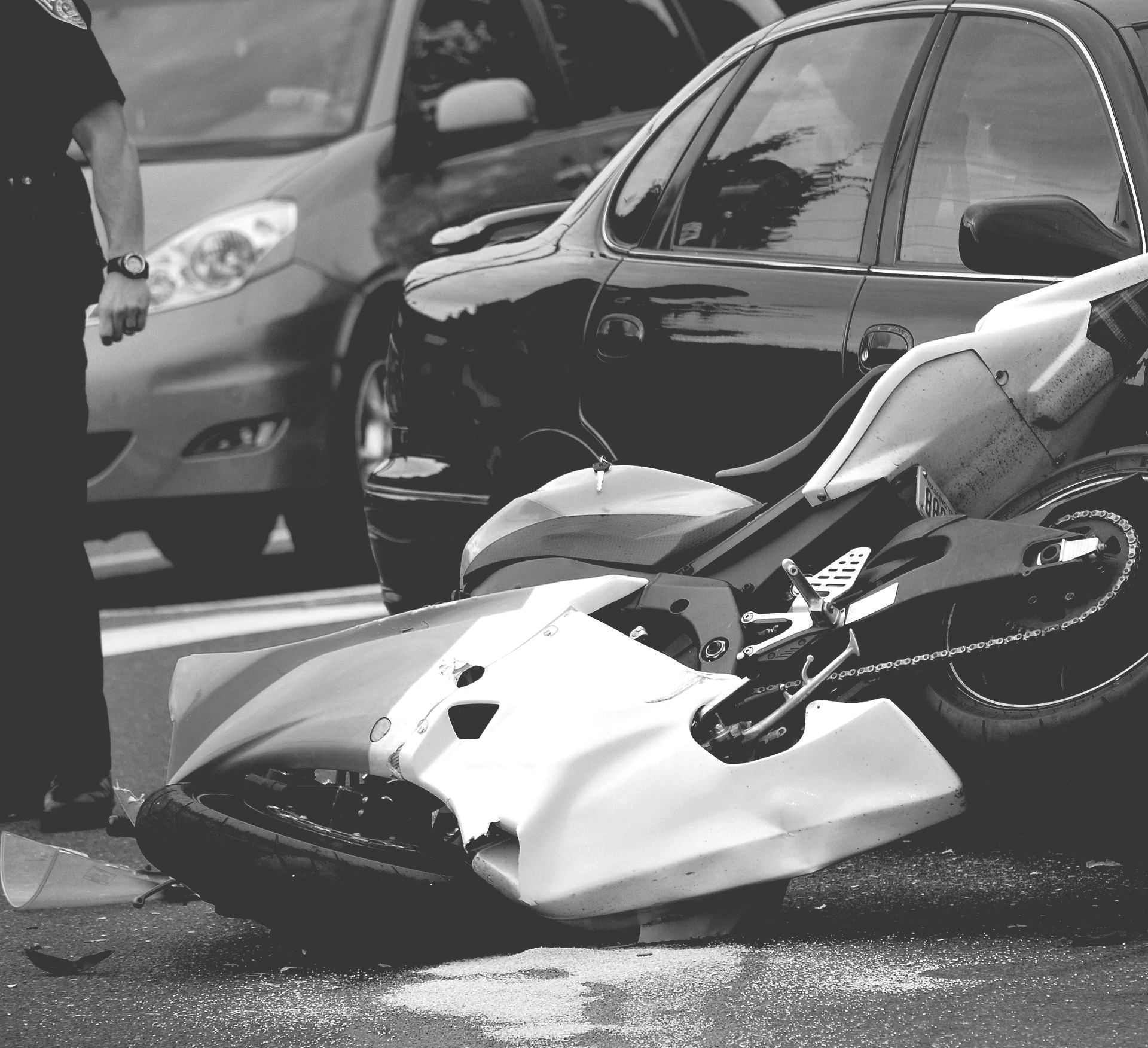 Motorcycle crashed into a car on a city street, with the bike lying on its side.