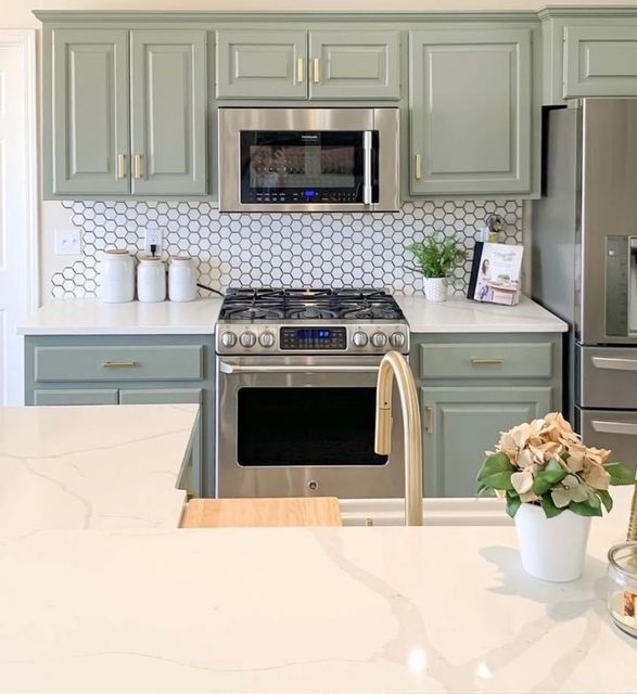Modern kitchen with mint cabinets, stainless steel appliances, white countertop, and a small flower vase