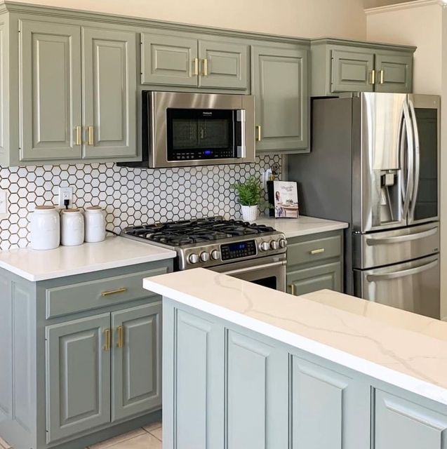 Modern kitchen with sage green cabinets, stainless appliances, white countertops, and a hexagon tile backsplash