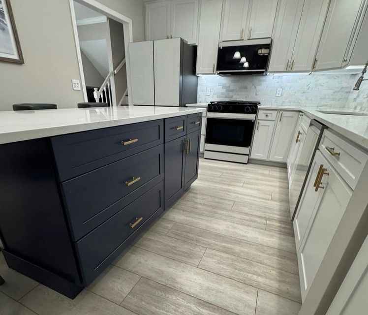 Modern white kitchen with navy island cabinets, stainless appliances, and light wood flooring
