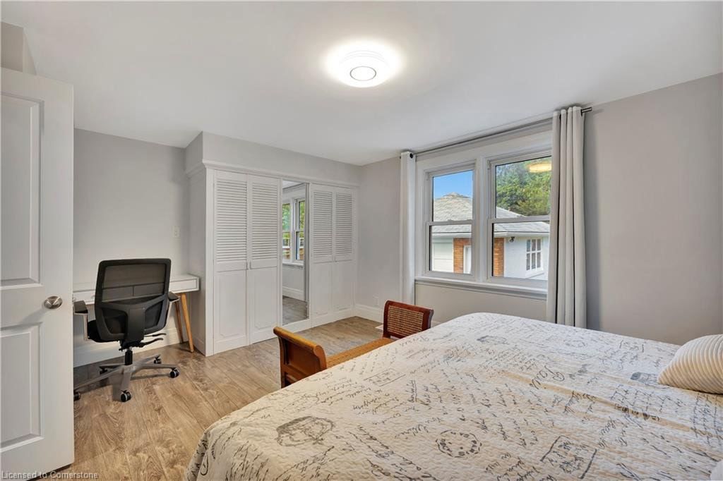 Bedroom with bed, desk, window, and closed closet doors. Light gray walls, wood-look floor.