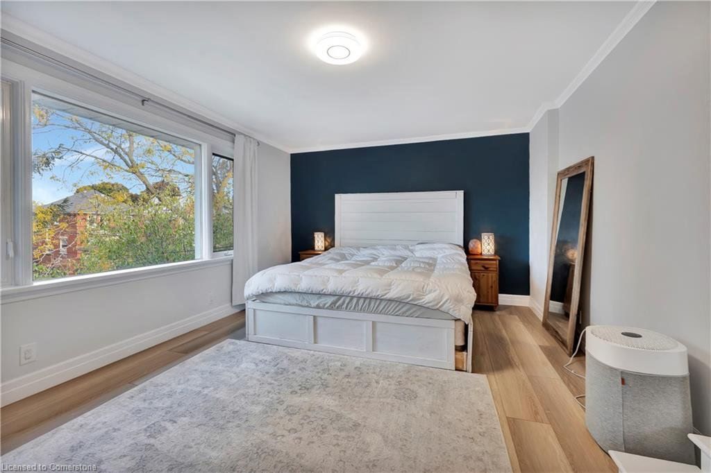 Bedroom with large window, blue accent wall, white bed, fluffy rug, wooden floors, and full-length mirror.