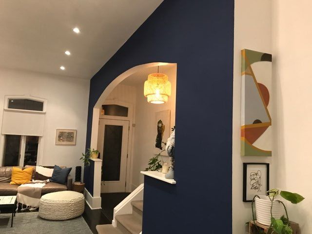 Interior with a navy accent wall, archway, and white trim. Modern art and a woven pendant light are featured.