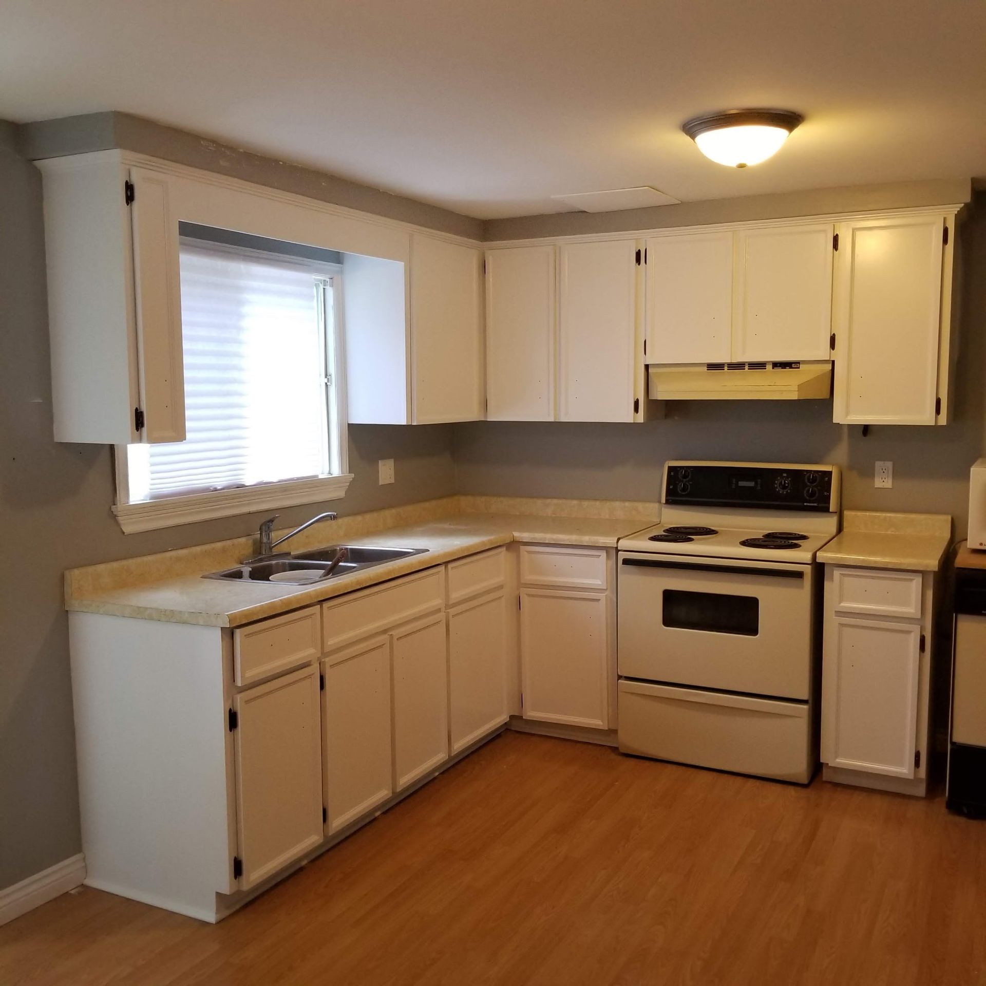 White kitchen cabinets and appliances; light countertops and wood floor.