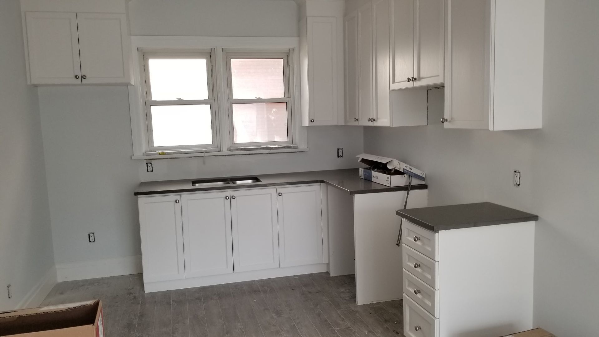 White kitchen cabinets with dark countertops. A window is in the center. The walls are light grey.