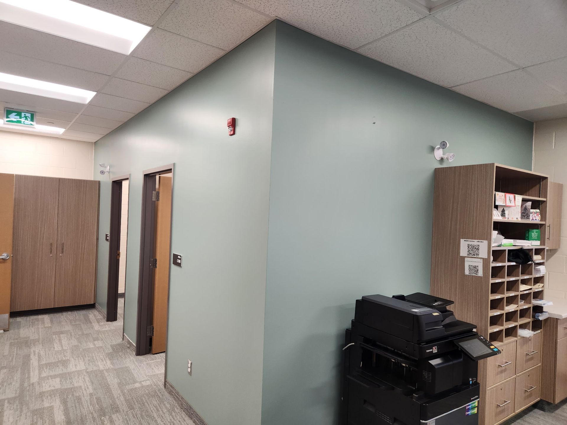 A hallway with green walls and wooden cabinets, a printer, and open doors.