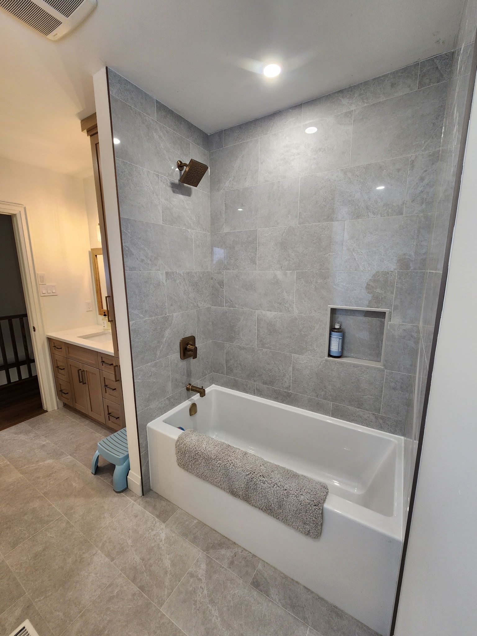 Bathroom with gray tile shower, white tub, brown fixtures, and a recessed shelf.