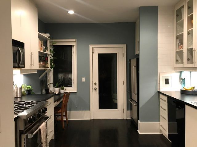 Kitchen with blue walls, white cabinets, dark floors, stainless steel appliances, and a door to the outside.