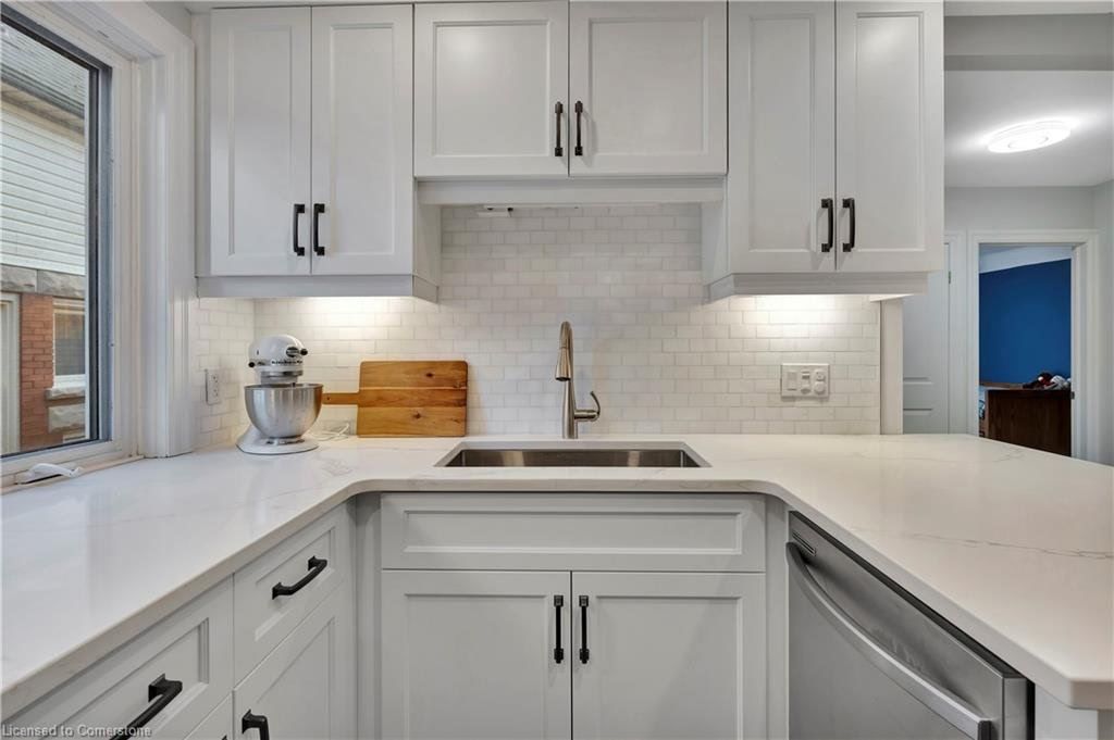 White kitchen with cabinets, sink, and countertop. Features include black hardware, backsplash, and a window.
