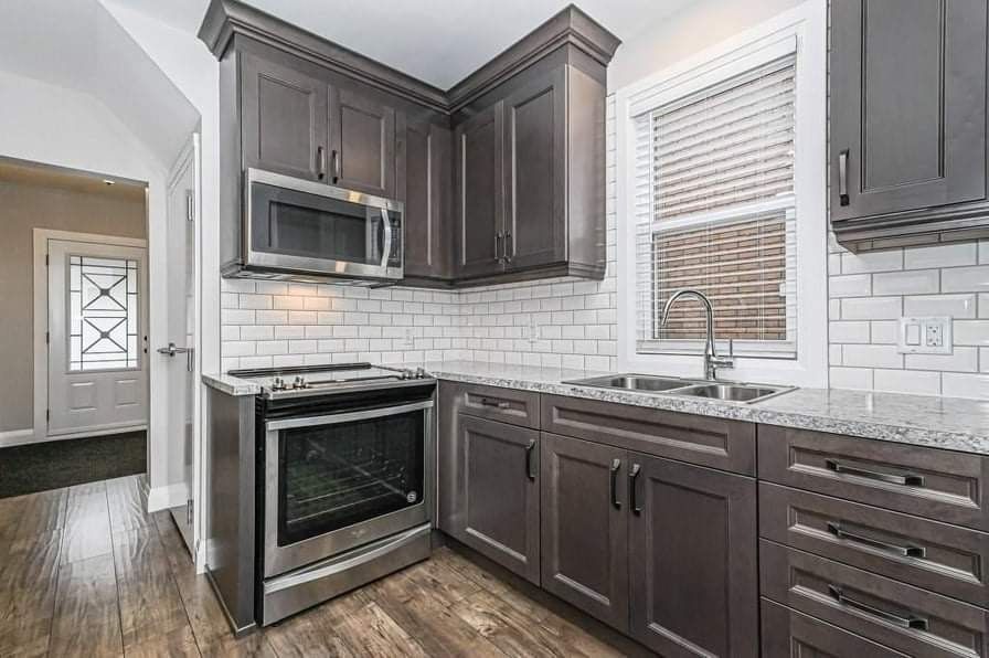 Kitchen with dark gray cabinets, stainless steel appliances, white subway tile, and a window.