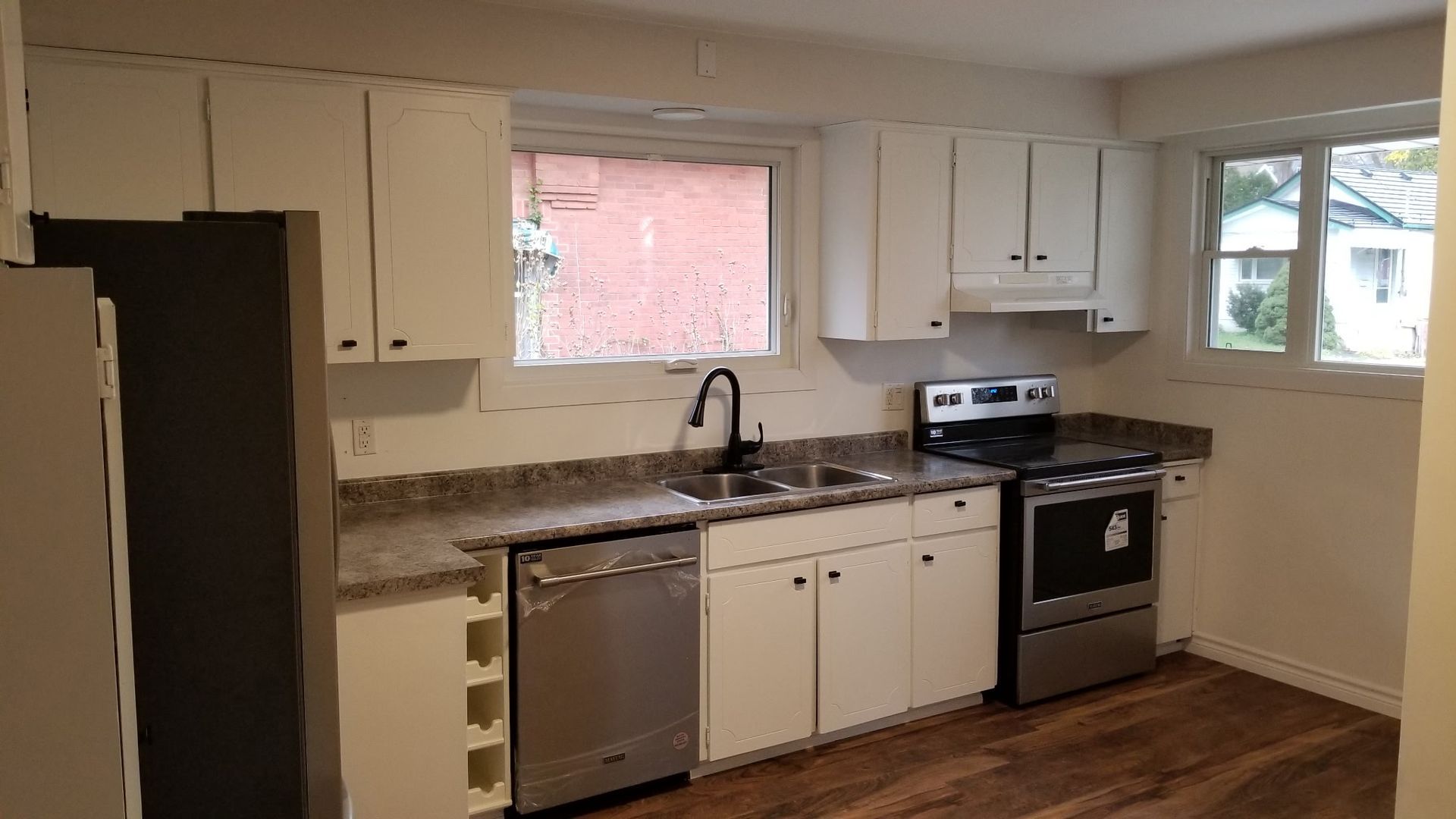 Kitchen with white cabinets, stainless steel appliances, granite countertops, and wood-look flooring.
