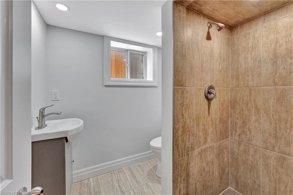 Bathroom interior with shower stall, sink, and toilet, featuring light-colored walls and wood-look flooring.