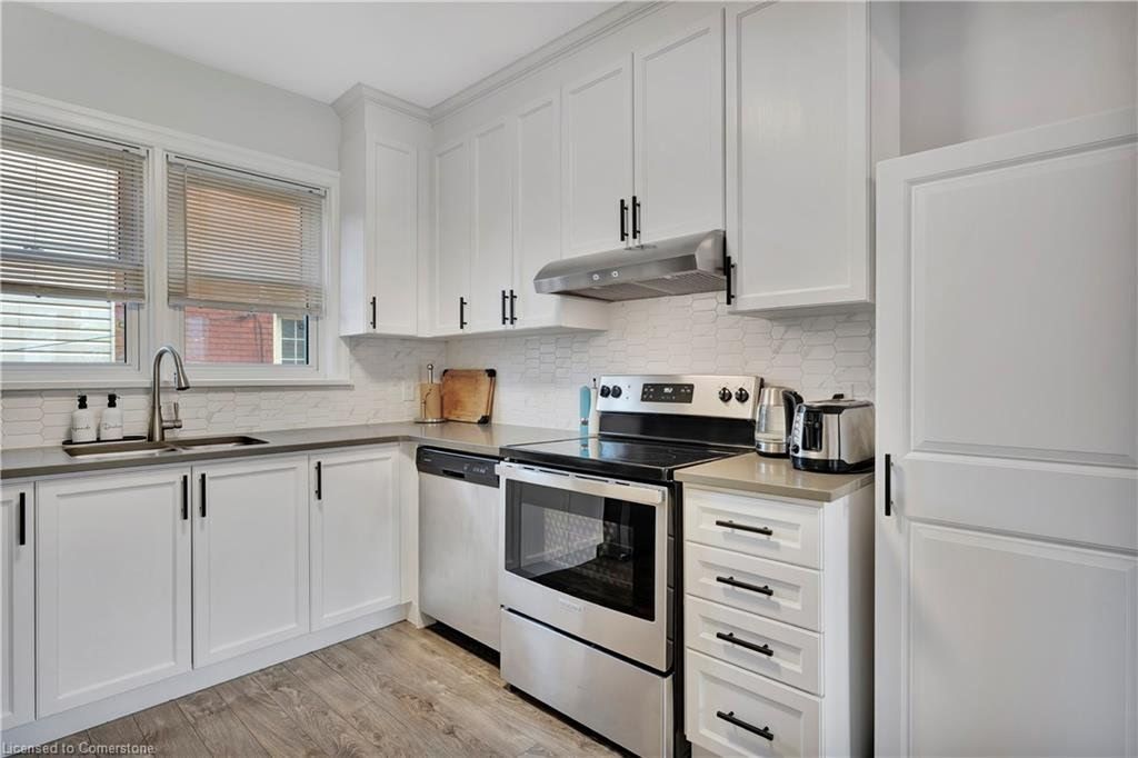 White kitchen with stainless steel appliances, cabinets, and a window with striped blinds.