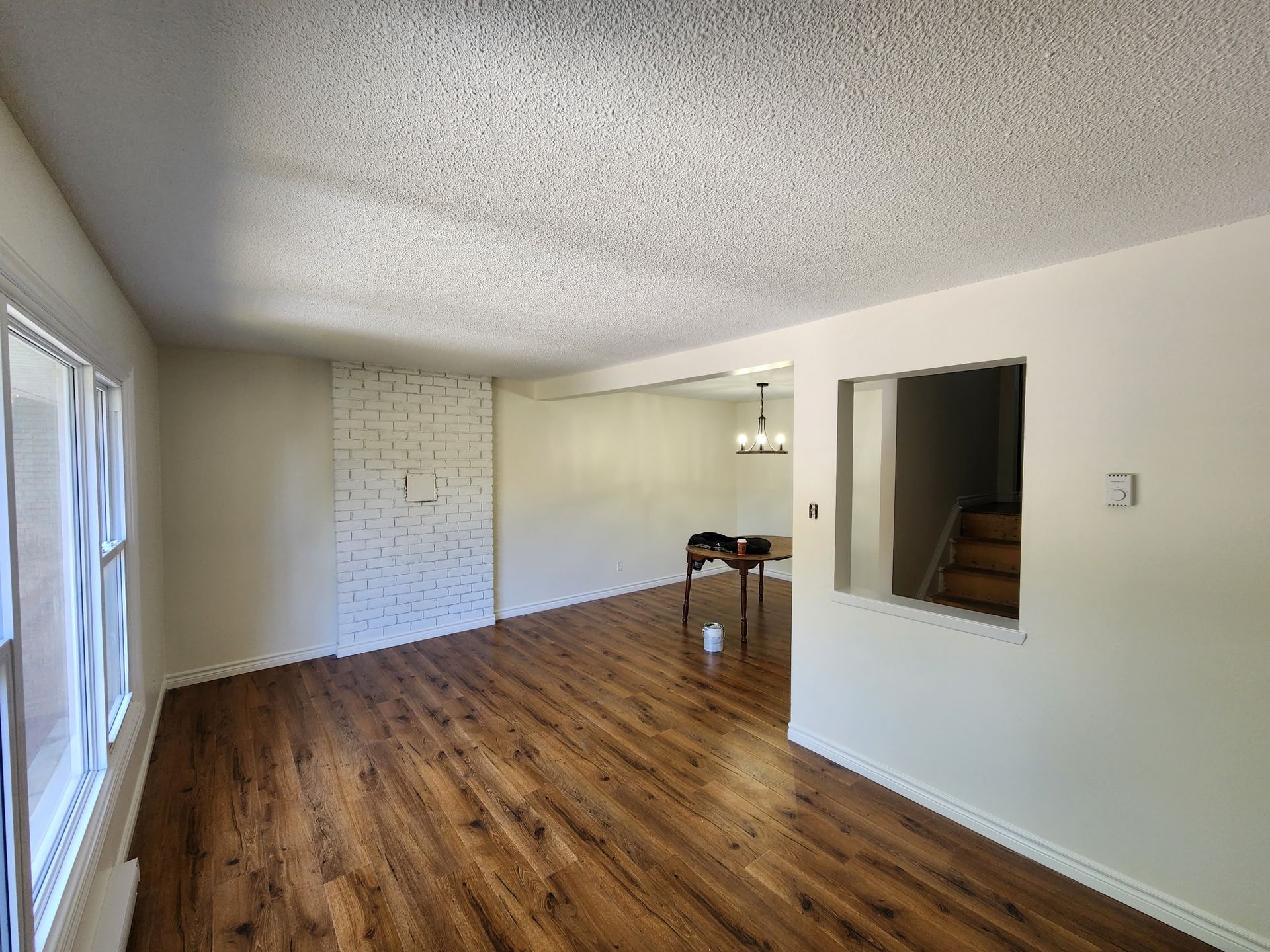 Empty living room with wood-look flooring, white walls, and a textured ceiling. Features a brick fireplace and a doorway.
