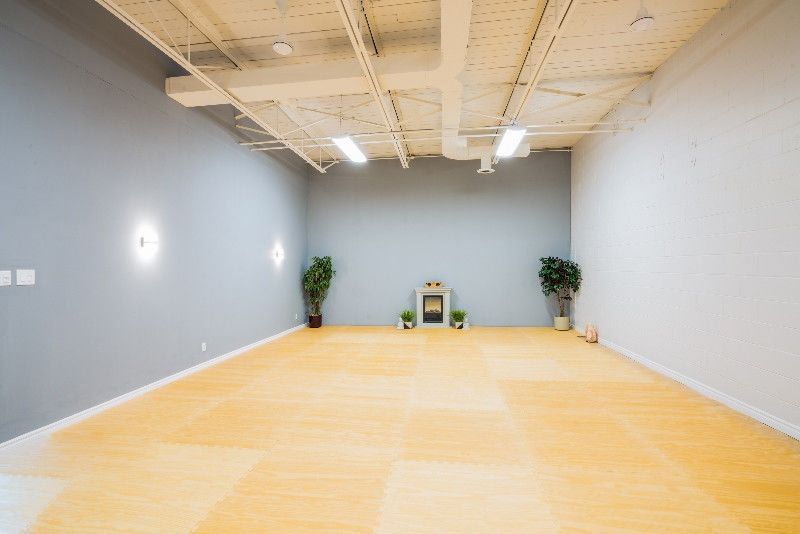 Empty yoga studio with light wooden floor, gray walls, and plants.