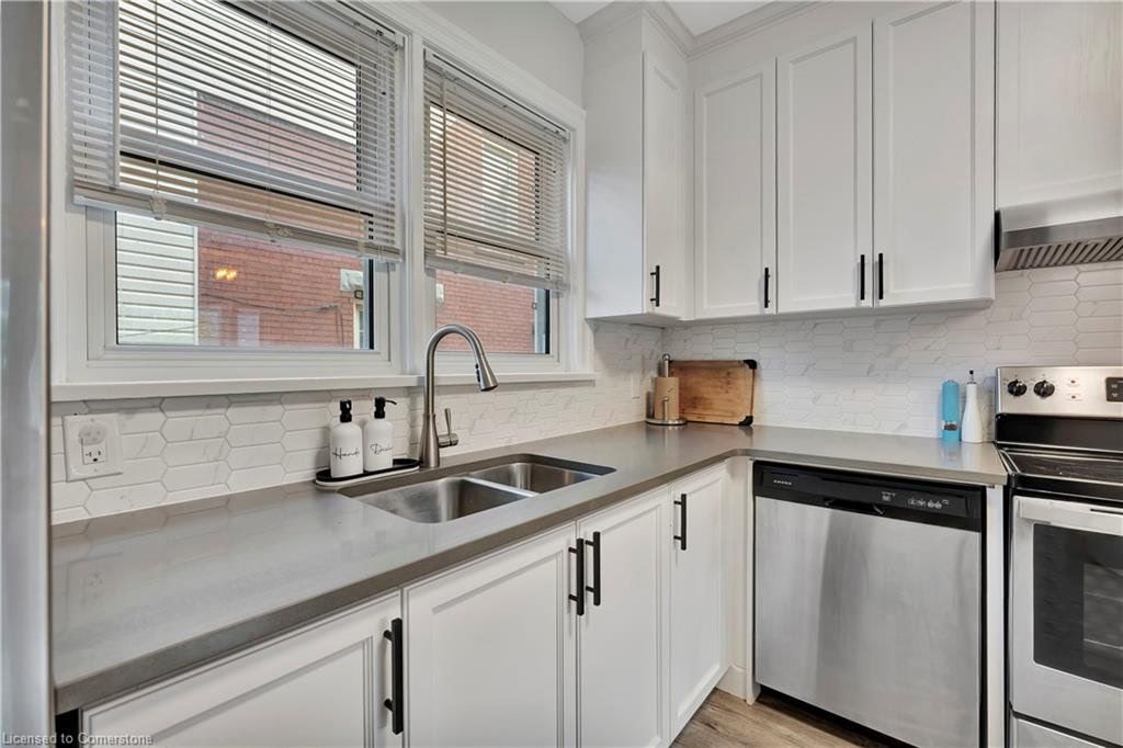 White kitchen with gray countertops, stainless steel appliances, and two windows with blinds.