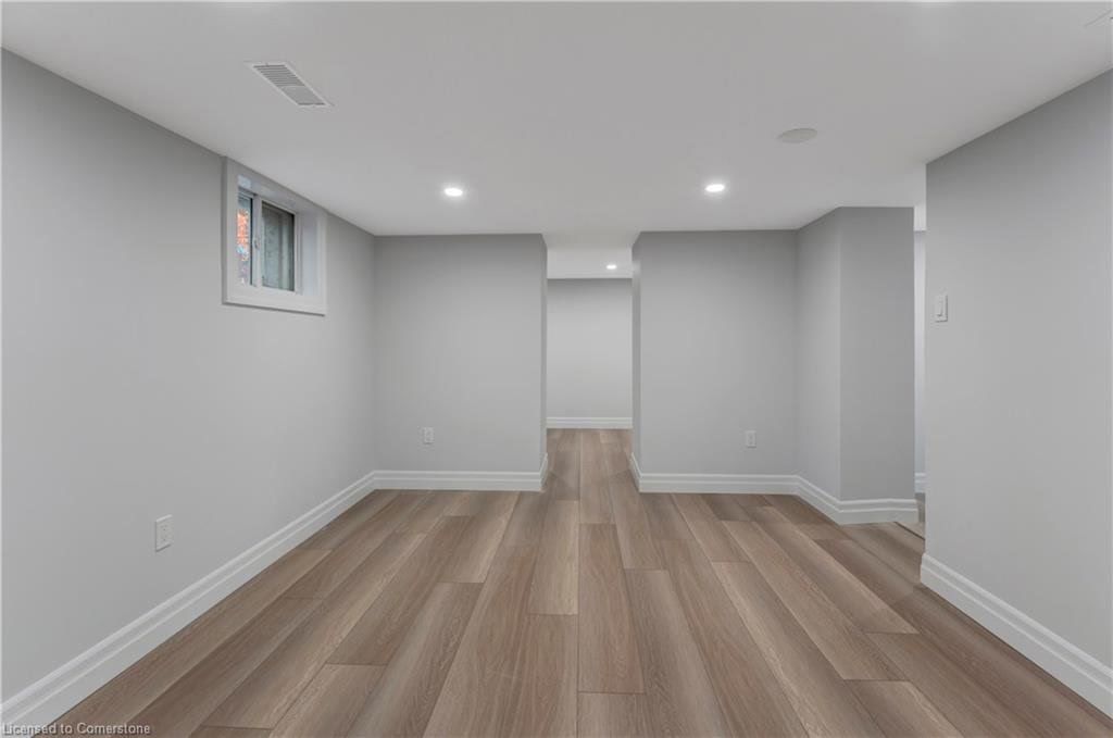 Empty finished basement with light gray walls, wood-look flooring, and recessed lighting.