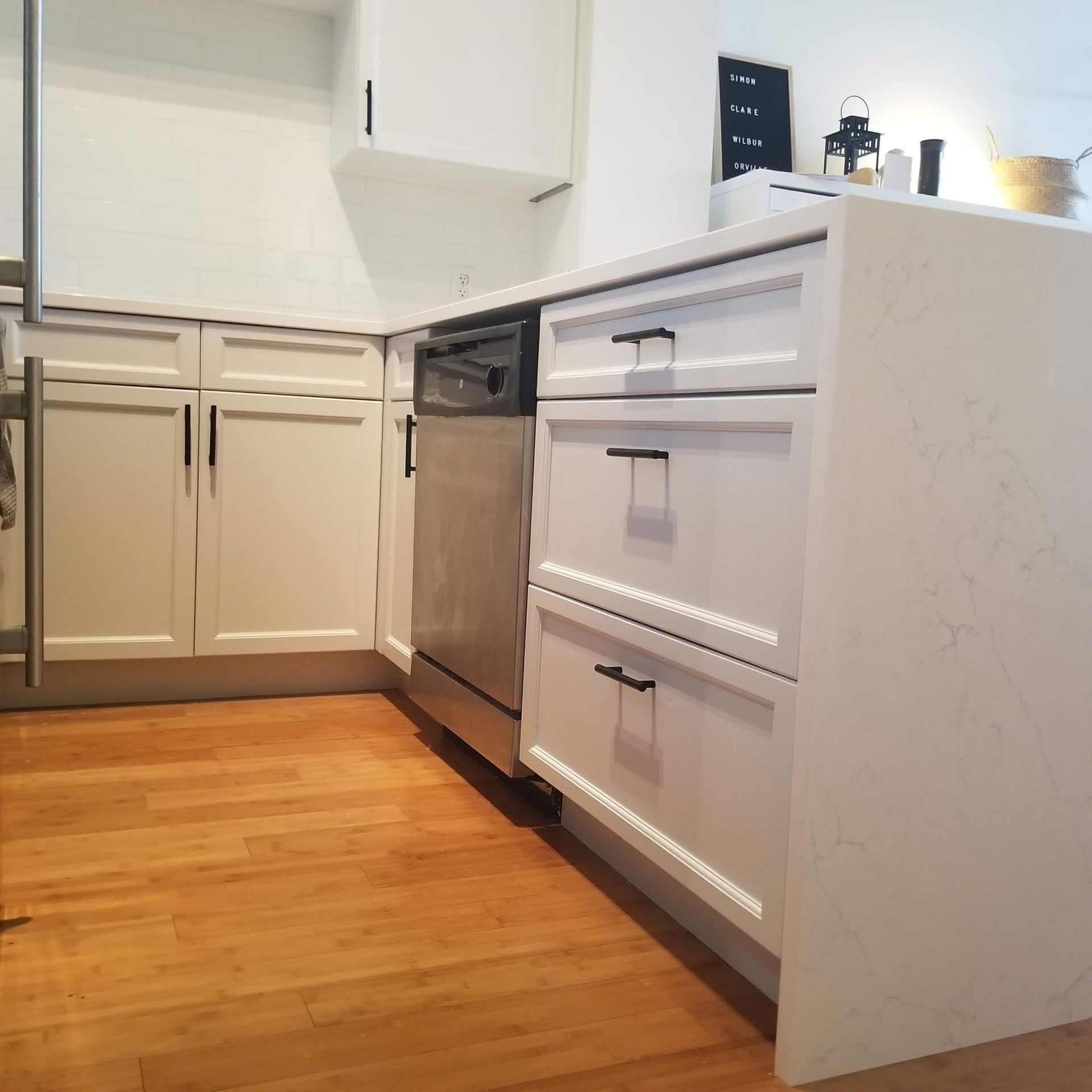 White kitchen cabinets, drawers, dishwasher, and wood floor.