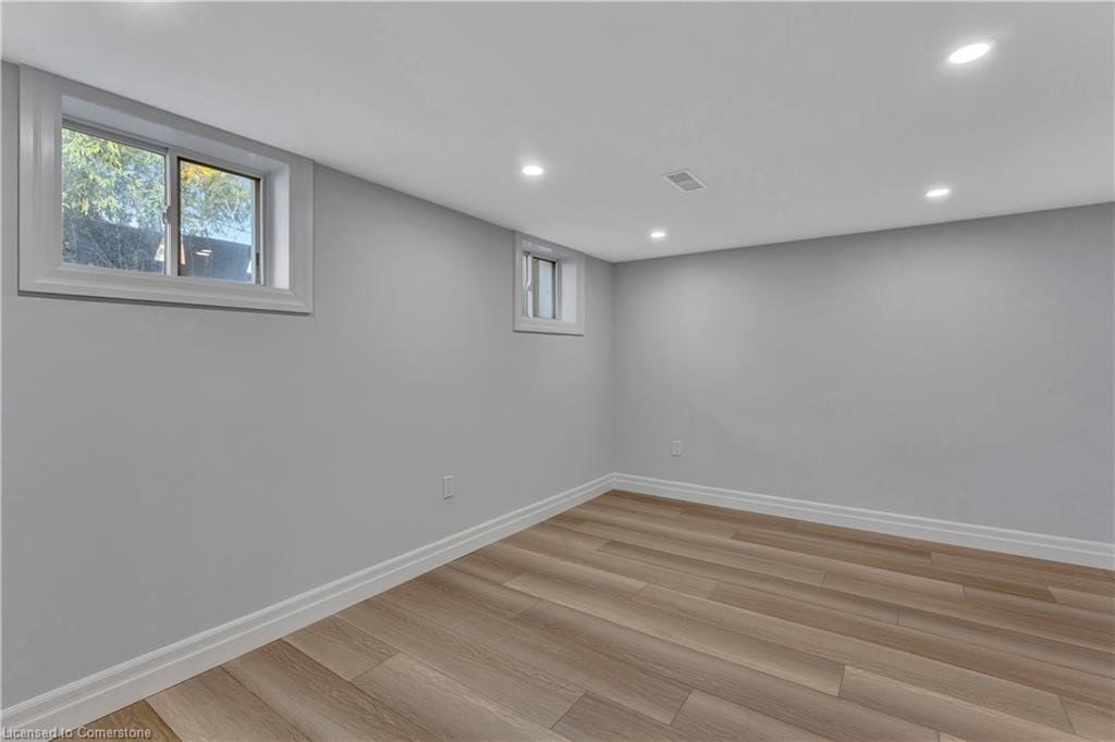 Empty room with gray walls, wood floor, two small windows, and recessed lighting.