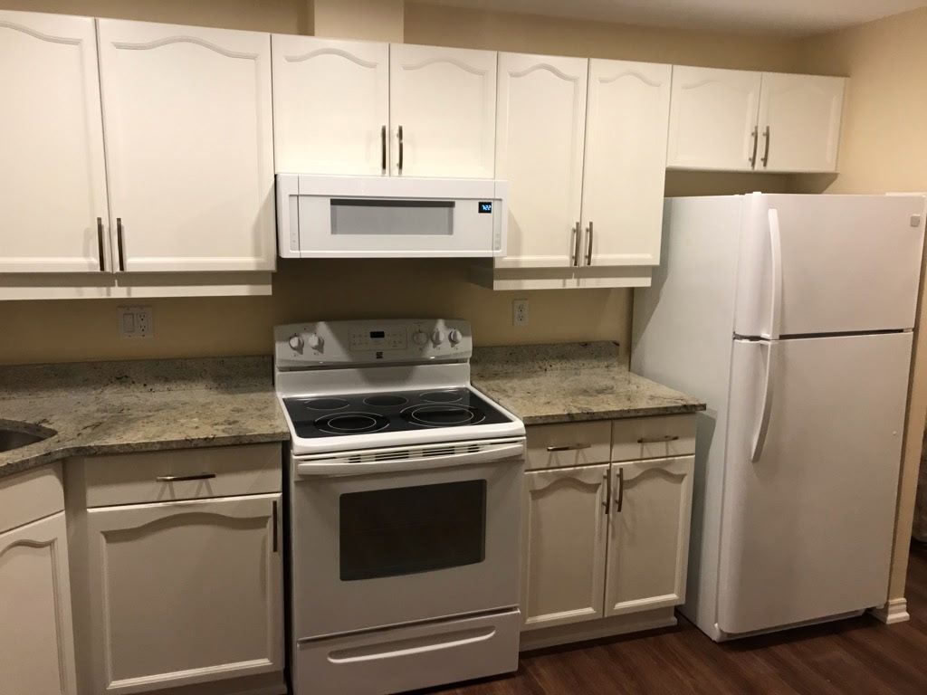 White kitchen with cabinets, stove, microwave, and refrigerator. Granite countertops.