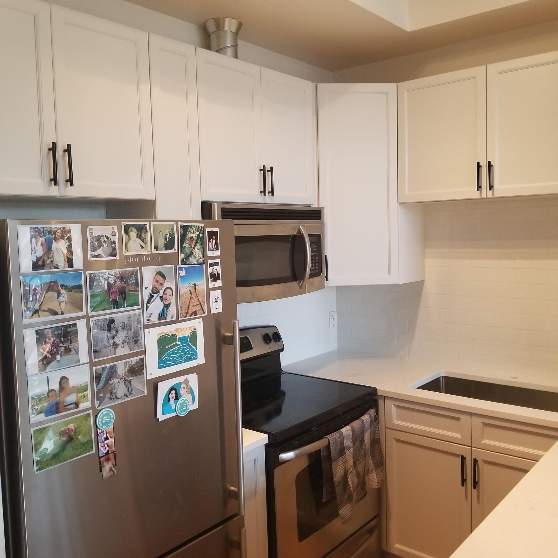 White kitchen with stainless steel appliances, upper and lower cabinets, photos on refrigerator.