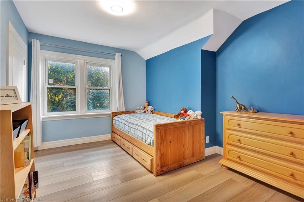 Child's bedroom with blue walls, wooden furniture, and a window. Light wood floor and a bed with toys.