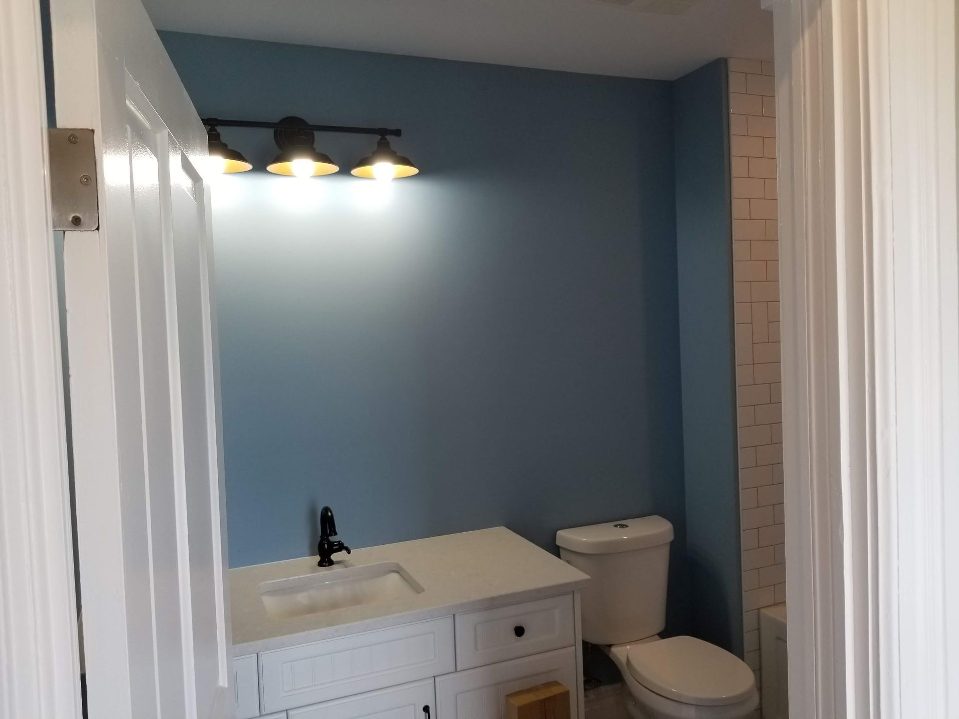 Bathroom with blue walls, white vanity, and black faucet. Lit by a three-bulb light fixture.