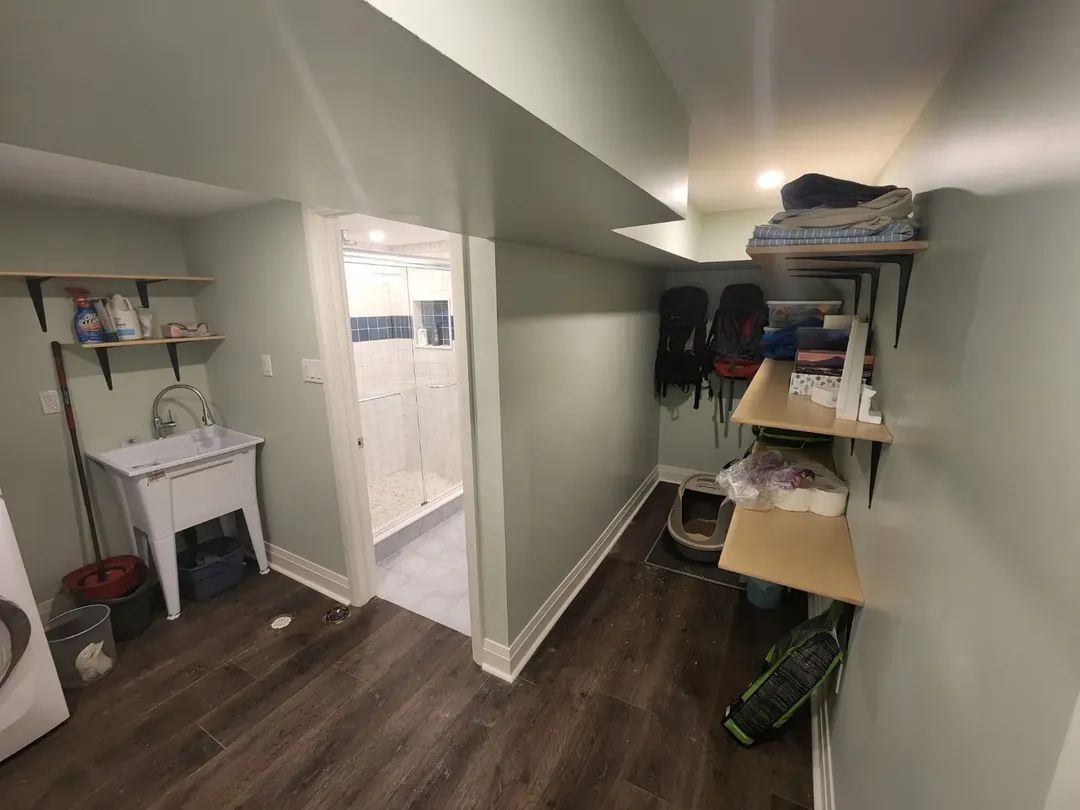 Basement utility room with shelves, sink, washer, and doorway. Wooden floor and light green walls.
