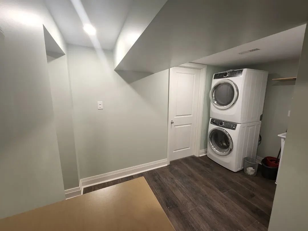 Laundry room with stacked washer/dryer, white door, and light green walls.