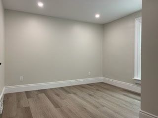 Empty room with light gray walls, white baseboards, and wood-look flooring. Two recessed lights.