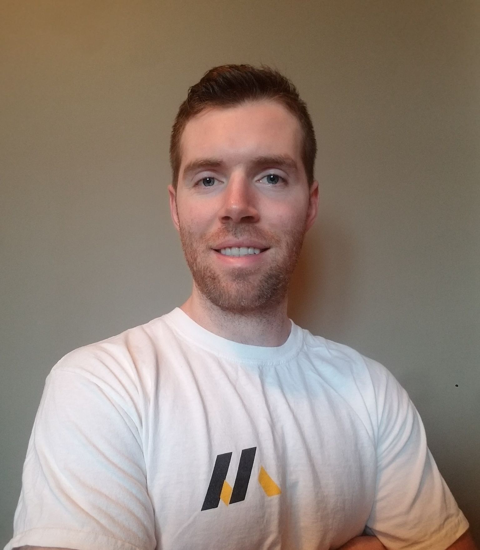 Man in white t-shirt with logo smiling in front of a neutral wall.