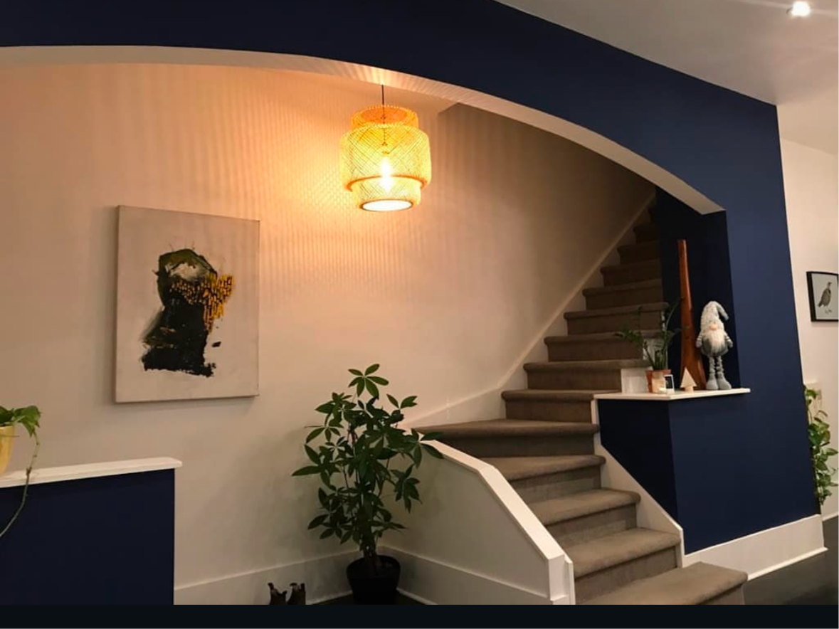 Staircase with navy blue accent walls, off-white walls, artwork, and a hanging light fixture.