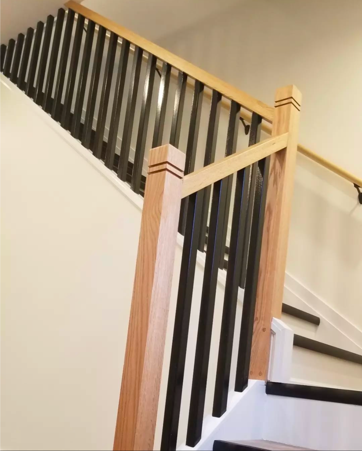 Wooden staircase with black balusters and light-colored handrails and posts.